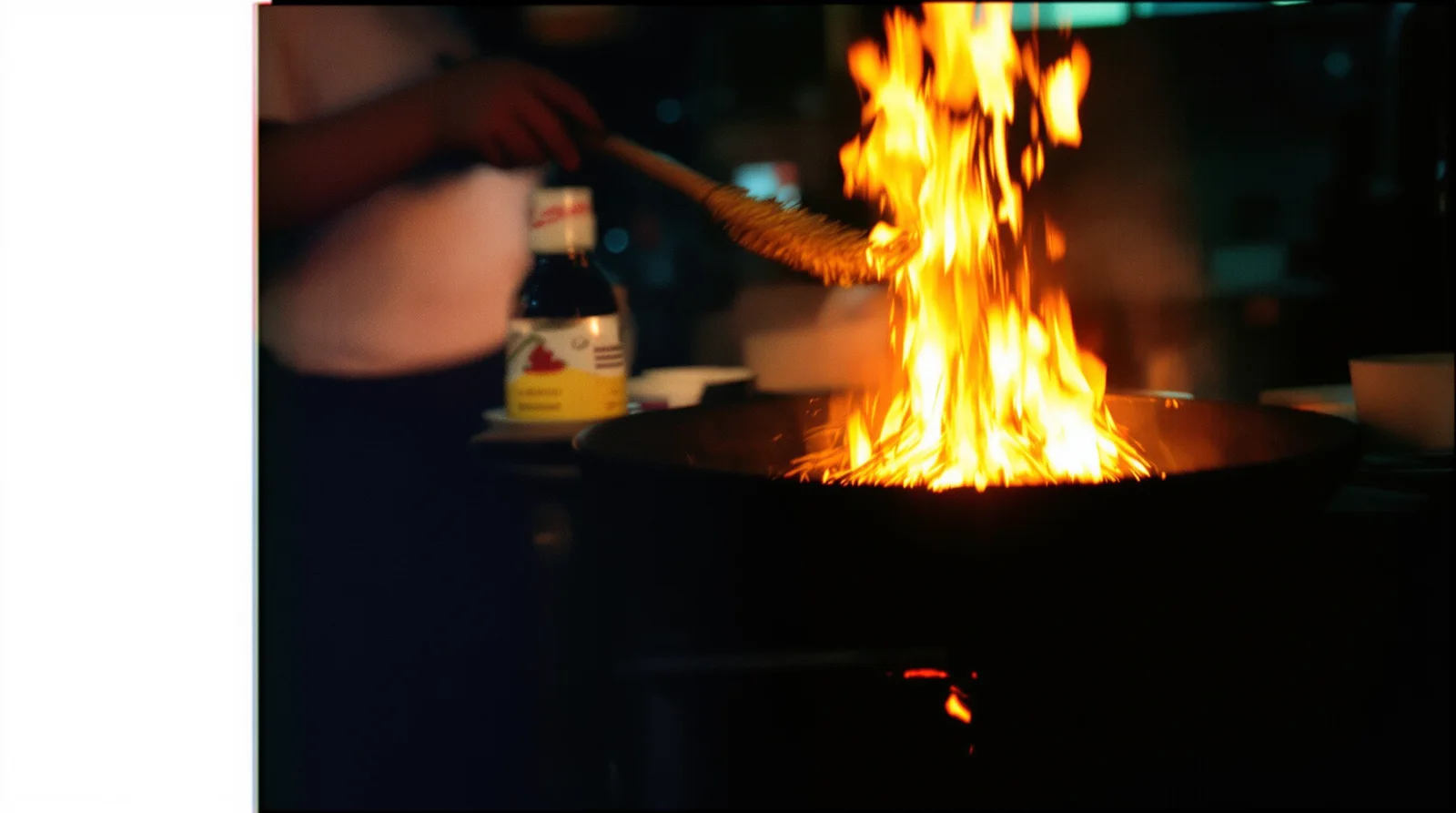 Street-food vendor in Bangkok flipping noodles in a flaming wok at night, motion blur on the flames, 35mm film look.